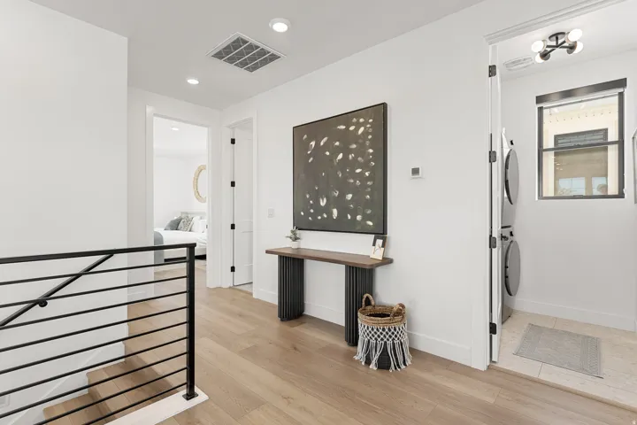 Wood-finish flooring, recessed lighting, contemporary black metal railing, laundry area with stacked appliances, and a window with a black frame