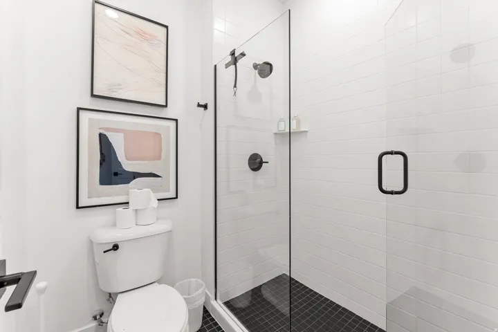 Glass-enclosed shower with matte black fixtures, white subway tile walls, and dark tile flooring