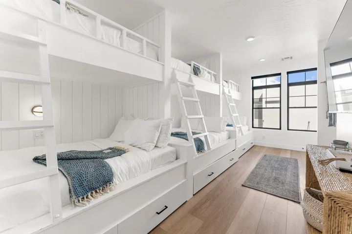 Built-in bunk beds with integrated storage drawers, wood-finish flooring, white shiplap wall paneling, fixed windows with black frames, and recessed ceiling lighting