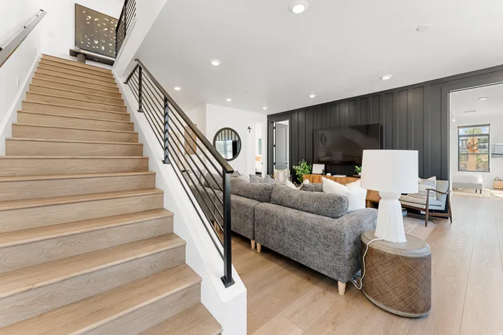 Wood-finish flooring throughout, modern black iron railing, recessed lighting, and a dark accent wall with vertical paneling