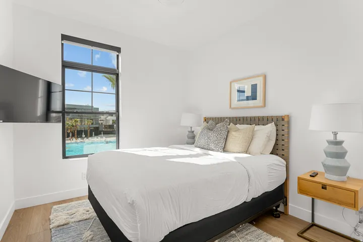 White walls, wood-finish flooring, black-framed window, and a woven headboard