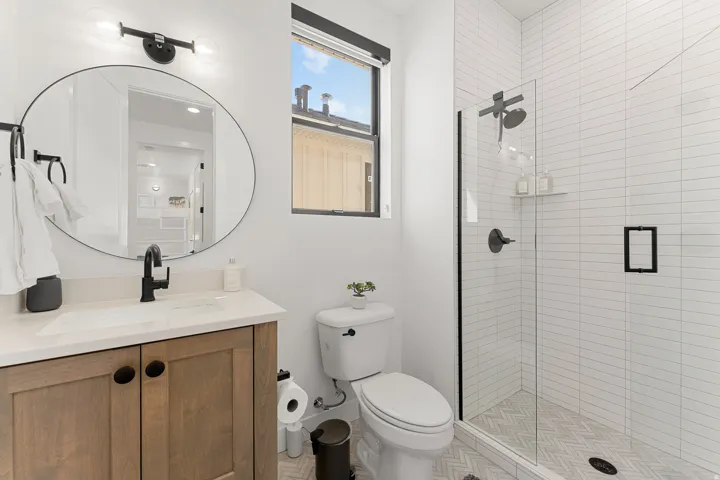 Wood-finish vanity with a light-toned countertop, matte black faucet, and oval mirror