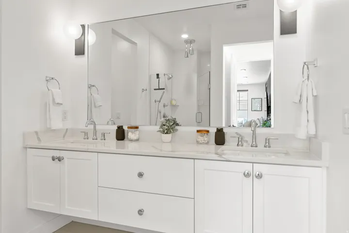 Dual vanity with white cabinetry, polished chrome fixtures, and a large integrated mirror