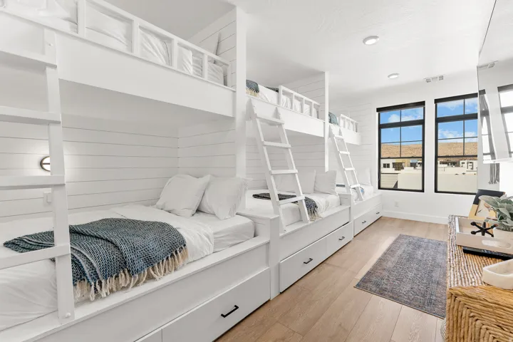 Built-in bunk beds with integrated storage drawers, shiplap wall accents, light wood-finish flooring, and black-framed windows