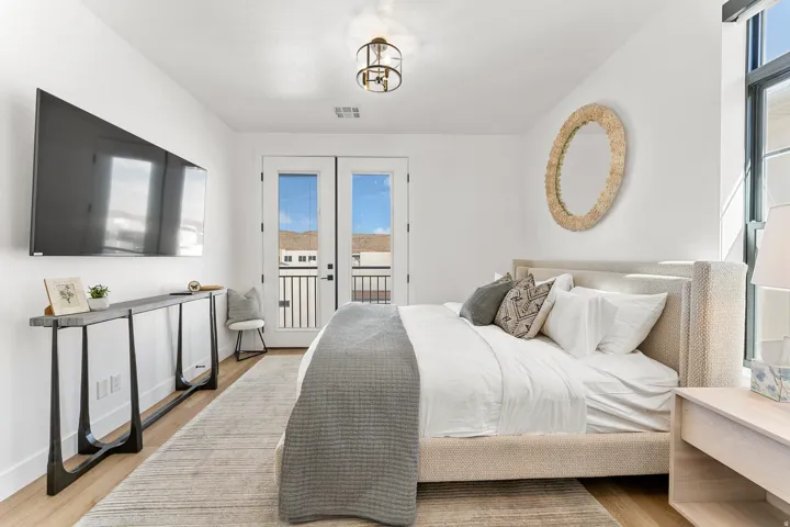 Wood-finish flooring with a neutral area rug, double French doors opening to a balcony, and a contemporary ceiling light fixture