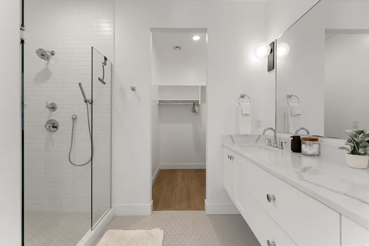 White subway tile shower with glass enclosure, dual vanity with undermount sinks, and a built-in closet system