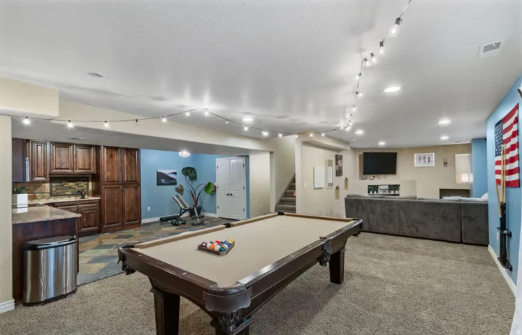 Spacious recreational area featuring a built-in wet bar with wood cabinetry, recessed lighting, and a neutral carpeted floor