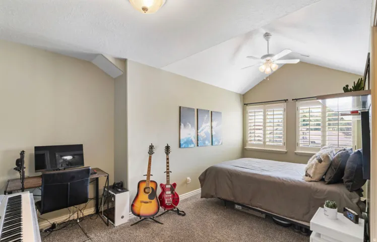 Vaulted ceiling with a ceiling fan light fixture, dual windows with plantation shutters, and textured carpeting