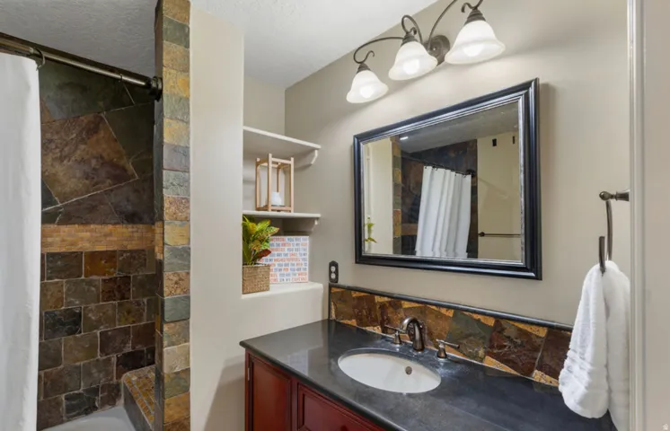 Tile shower enclosure with an integrated bench, dark countertop with an undermount sink, rich wood-finish vanity, and a framed mirror with overhead lighting
