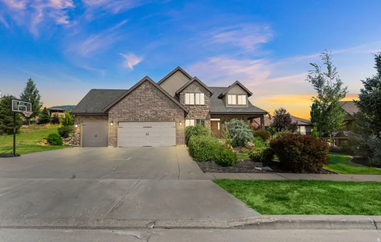 Brick and stone facade, covered entry, multiple dormer windows, attached two-car garage, and landscaped front yard