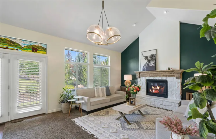 Vaulted ceilings, a stone-surround fireplace with a wood mantel, and a prominent chandelier