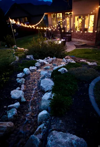 Landscaped backyard featuring a stone-lined water feature, established plantings, and a paver patio