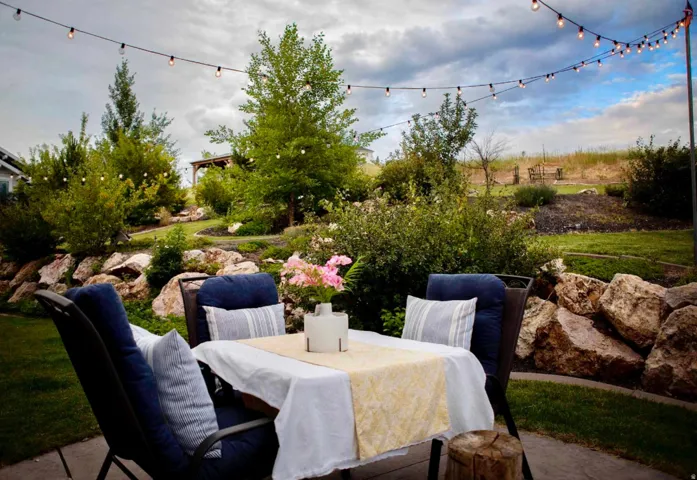 Patio area with string lighting, mature landscaping, and a rock retaining wall