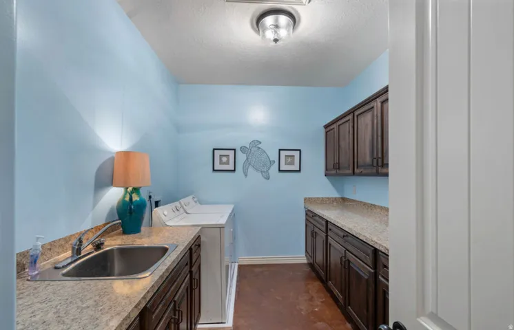Functional utility room featuring dark wood-finish cabinetry, light-toned countertops, a stainless steel sink, and durable flooring