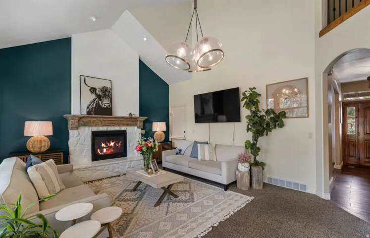 Vaulted ceilings, a stone fireplace with a carved wood mantel, and a modern light fixture enhance this living space