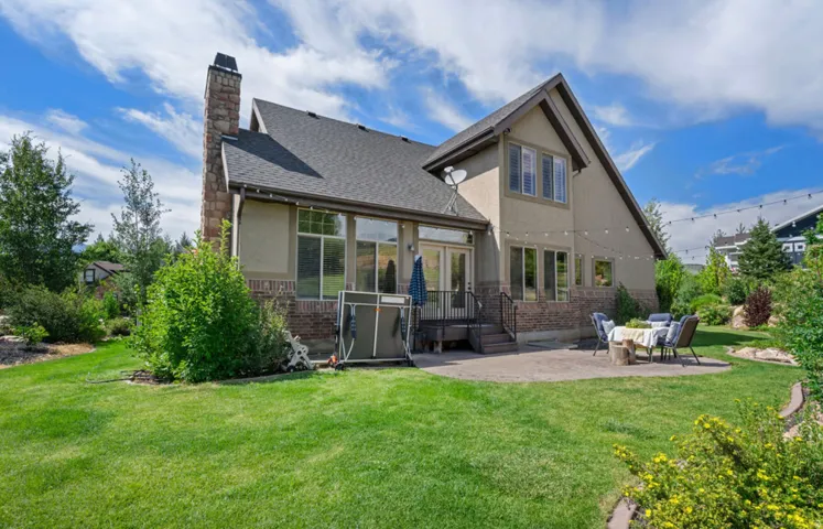 Expansive green lawn with mature landscaping, a stone-clad chimney, and a multi-level patio
