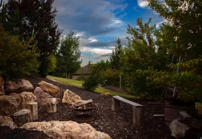 Terraced landscaping featuring a fire pit, natural stone accents, mature trees, and a wooden bench