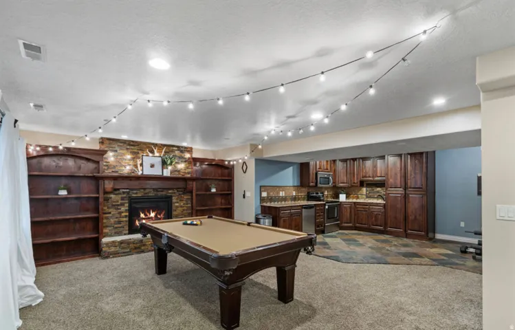 Stone-clad fireplace with a wood mantle, built-in shelving, full kitchen with dark wood cabinetry, stainless steel appliances, and slate-style tile flooring