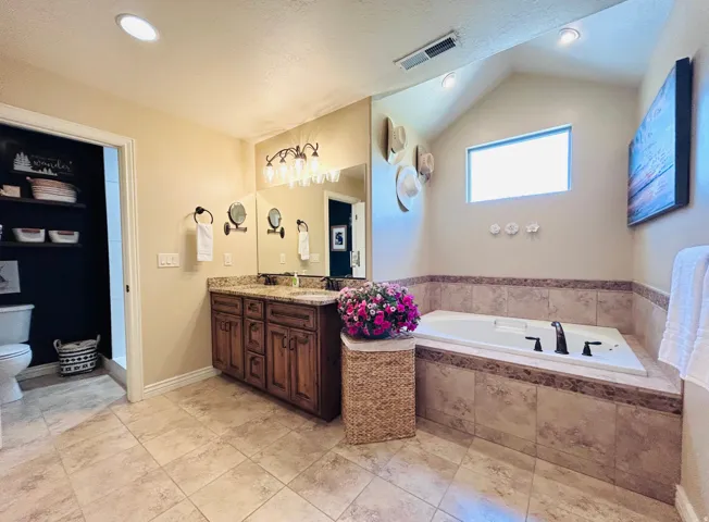 Spacious bathroom featuring a dual vanity with a granite-style countertop, a large soaking tub with tiled surround, and recessed ceiling lighting