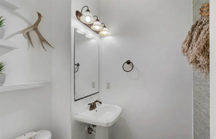 Pedestal sink with bronze-finish faucet, framed mirror with vanity lighting, and wall-mounted shelving