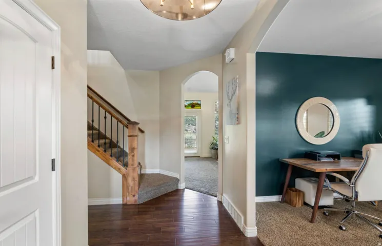 Dark wood-finish flooring, staircase with wood newel post and balusters, arched entryway, and a room with a deep teal accent wall