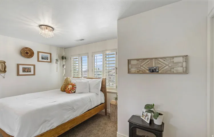 Bedroom featuring a crystal flush mount light fixture, plantation shutters, and light-colored carpet