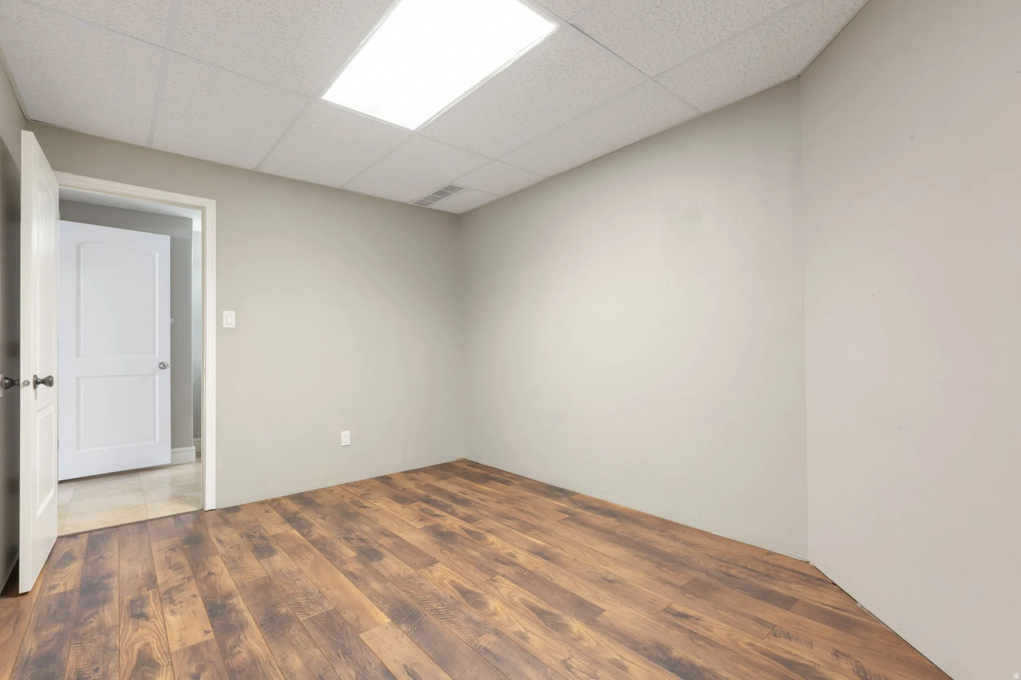 Wood-finish flooring, drop ceiling with integrated lighting, and neutral wall tones