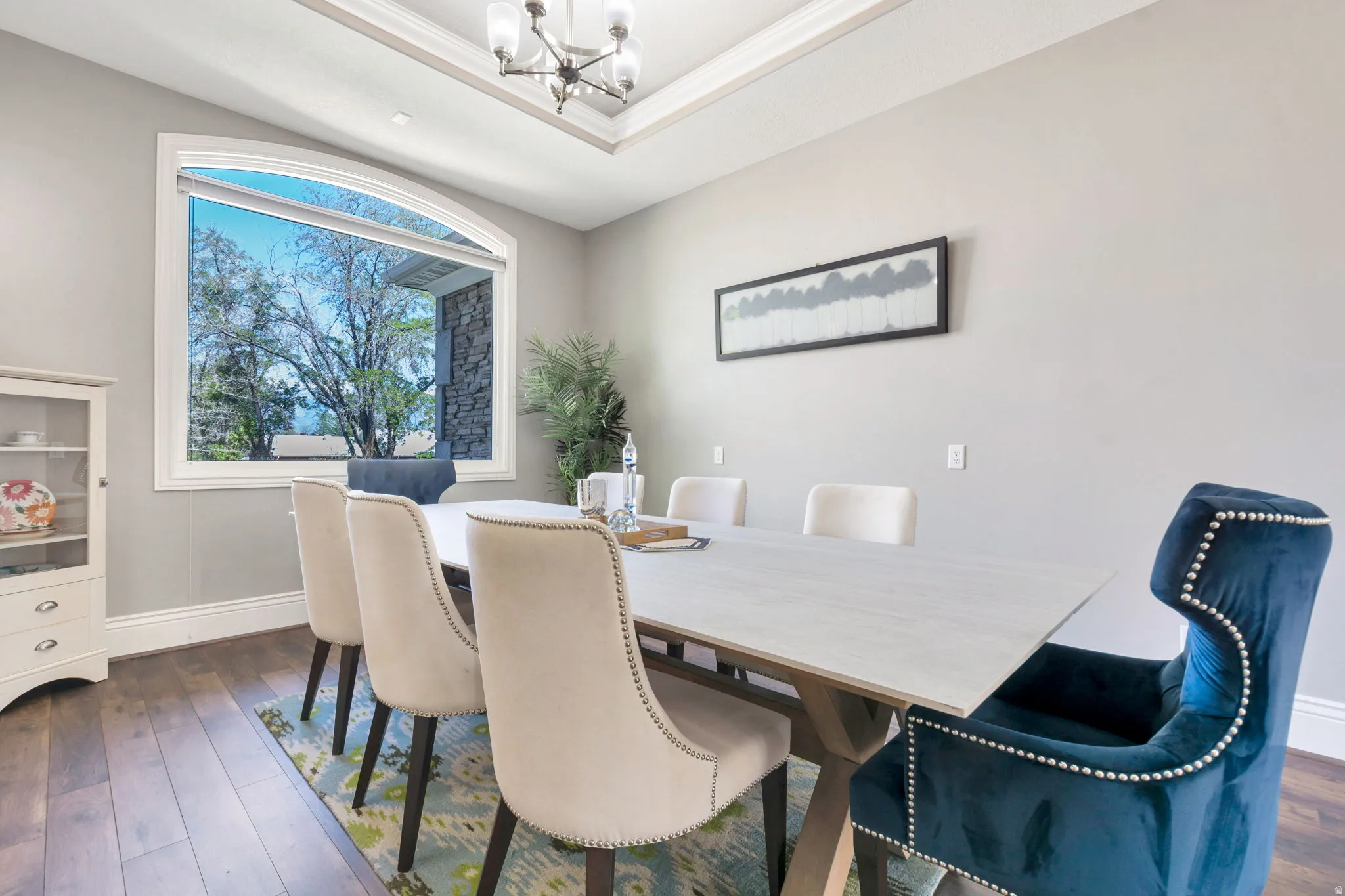 Arched window with broad white trim, wood-finish flooring, tray ceiling, and a contemporary chandelier