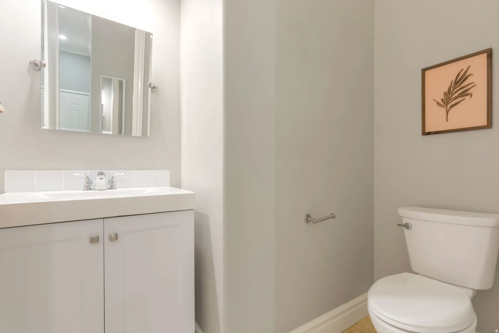 White vanity with integrated sink, chrome faucet, wall-mounted mirror, and a white toilet