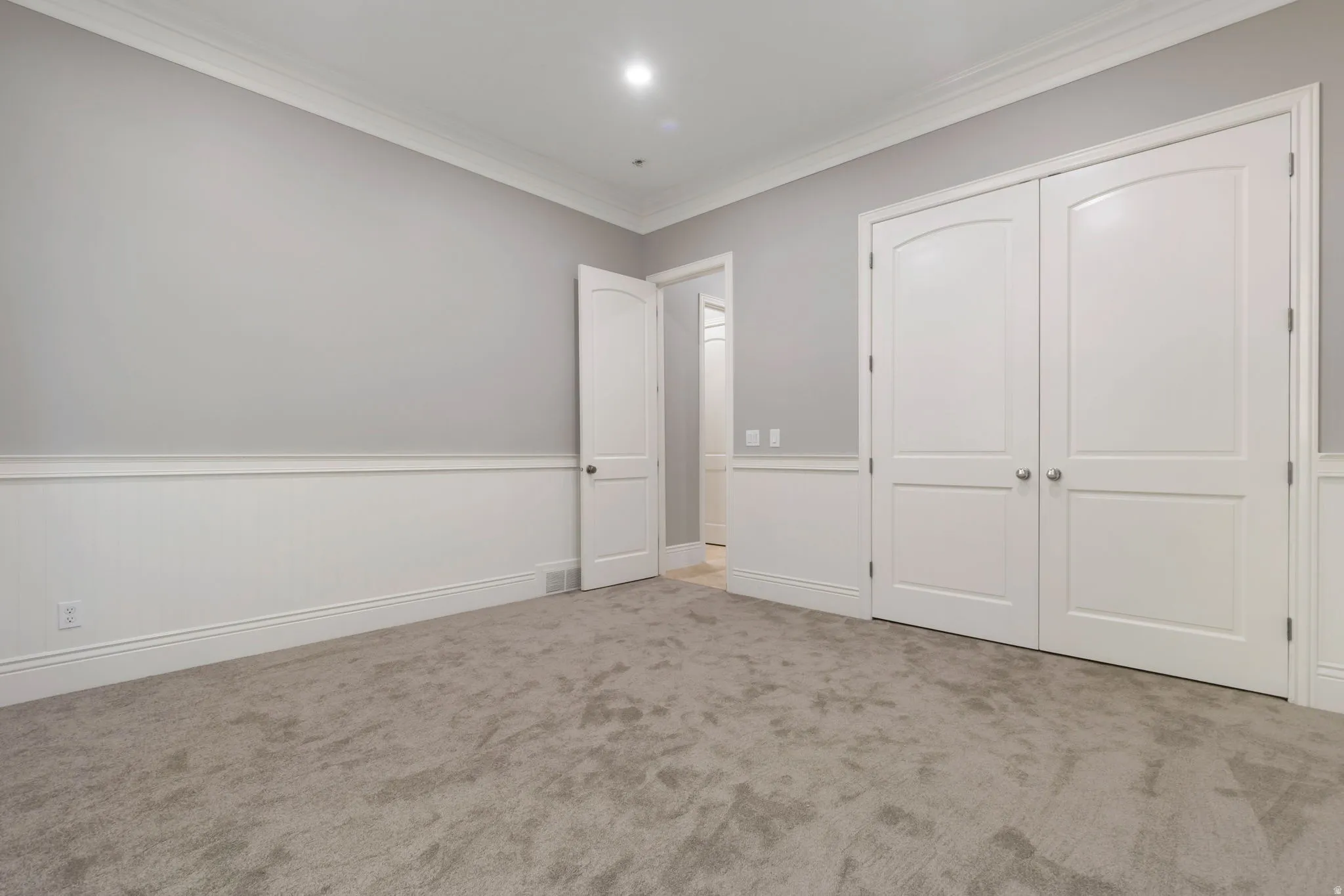 Plush grey carpeting, crisp white wainscoting, elegant crown molding, and recessed lighting
