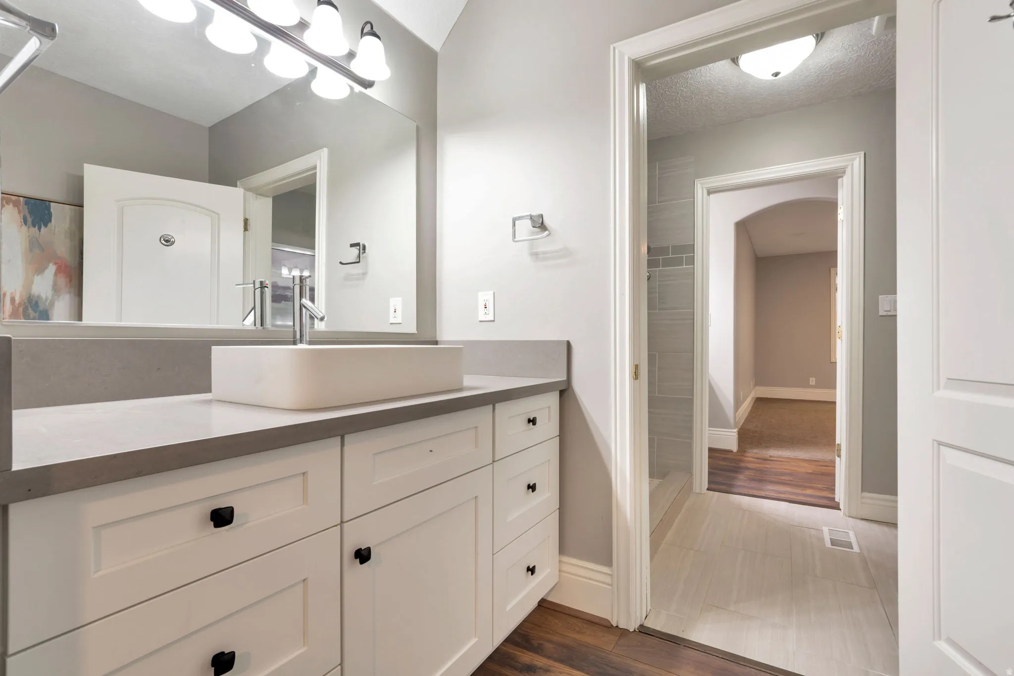 White vanity with black hardware, rectangular vessel sink, wall-mounted faucet, and a large mirror