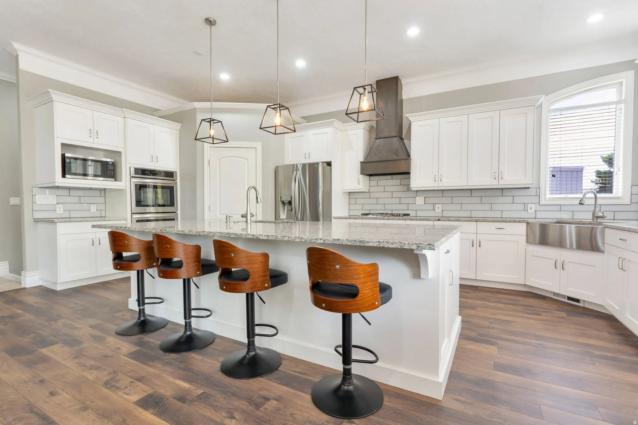 Spacious kitchen featuring an expansive central island with counter seating, light-toned countertops, white cabinetry, and wood-finish flooring