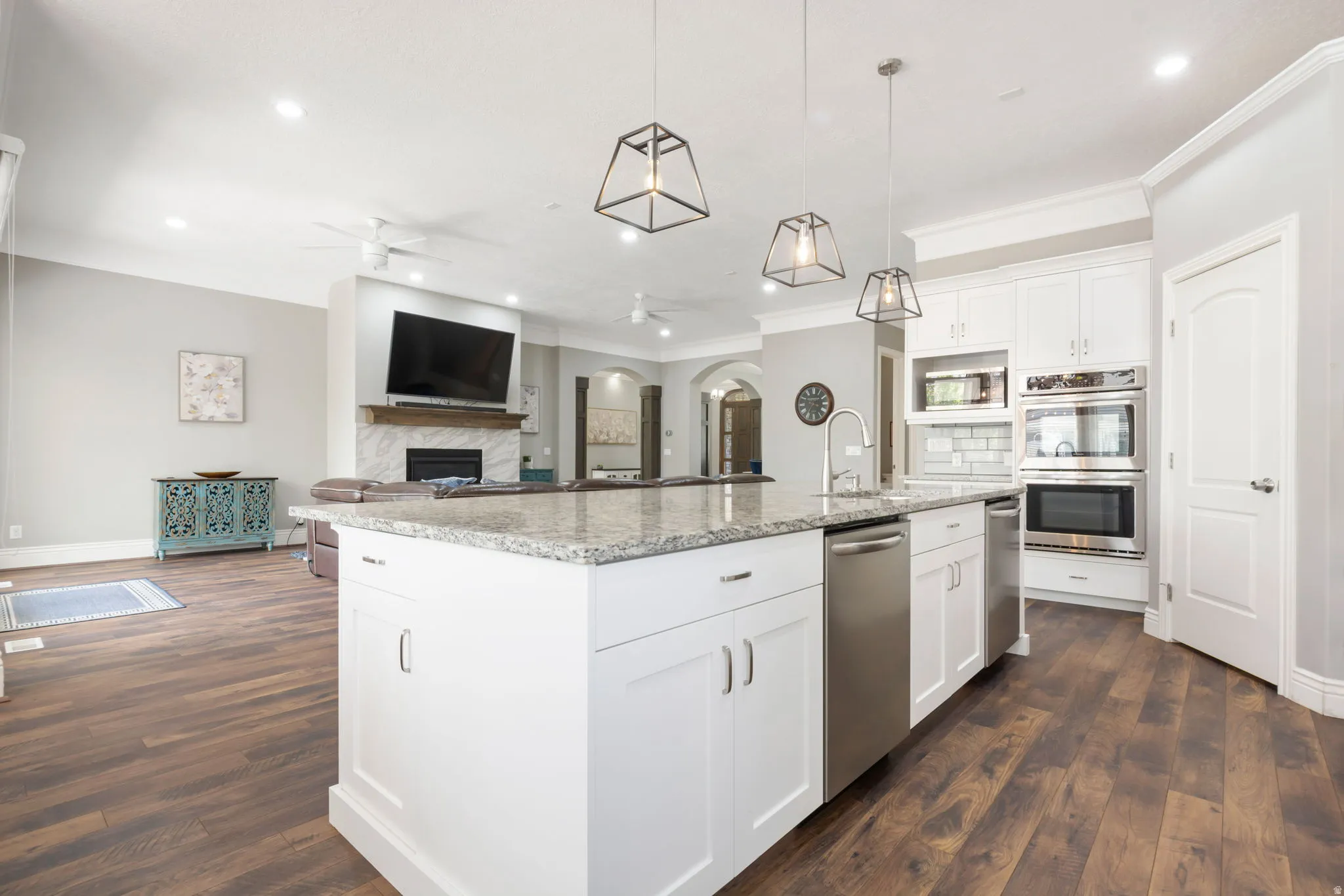 Spacious kitchen island with light-toned countertop, white cabinetry with silver-toned hardware, stainless steel dishwasher, and wood-finish flooring