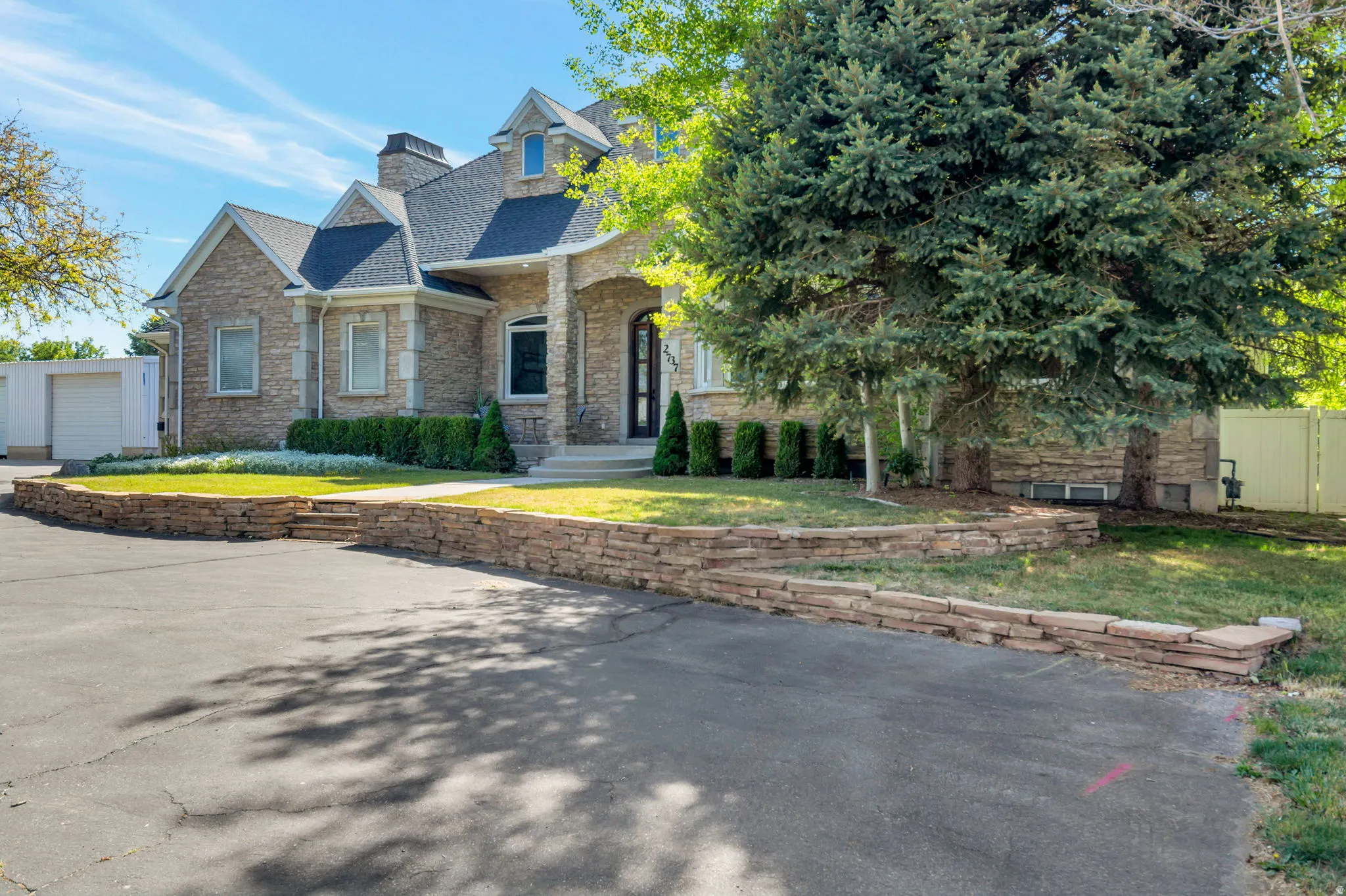 Stone exterior with contrasting trim, arched entryway, dormer windows, and a multi-level stone retaining wall