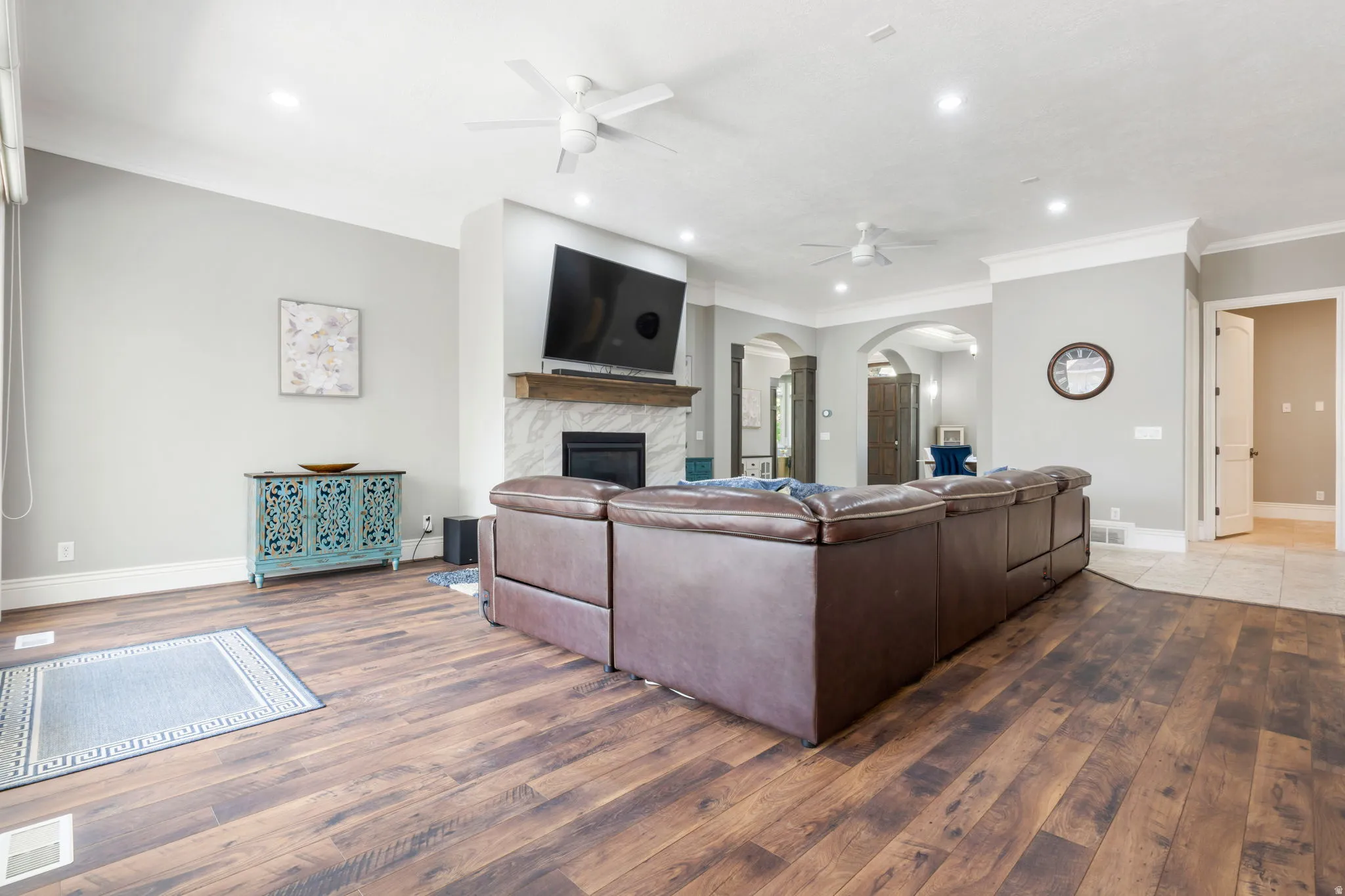 Spacious living area featuring wood-finish flooring, a fireplace with a tile surround and wood mantel, recessed lighting, and ceiling fans
