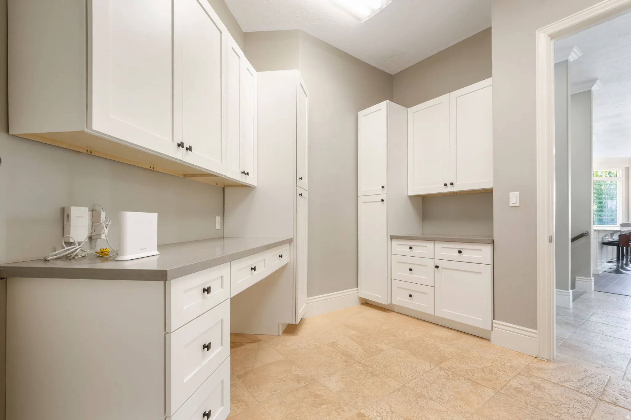 Built-in white cabinetry with dark hardware, integrated desk space, grey countertops, and neutral tile flooring