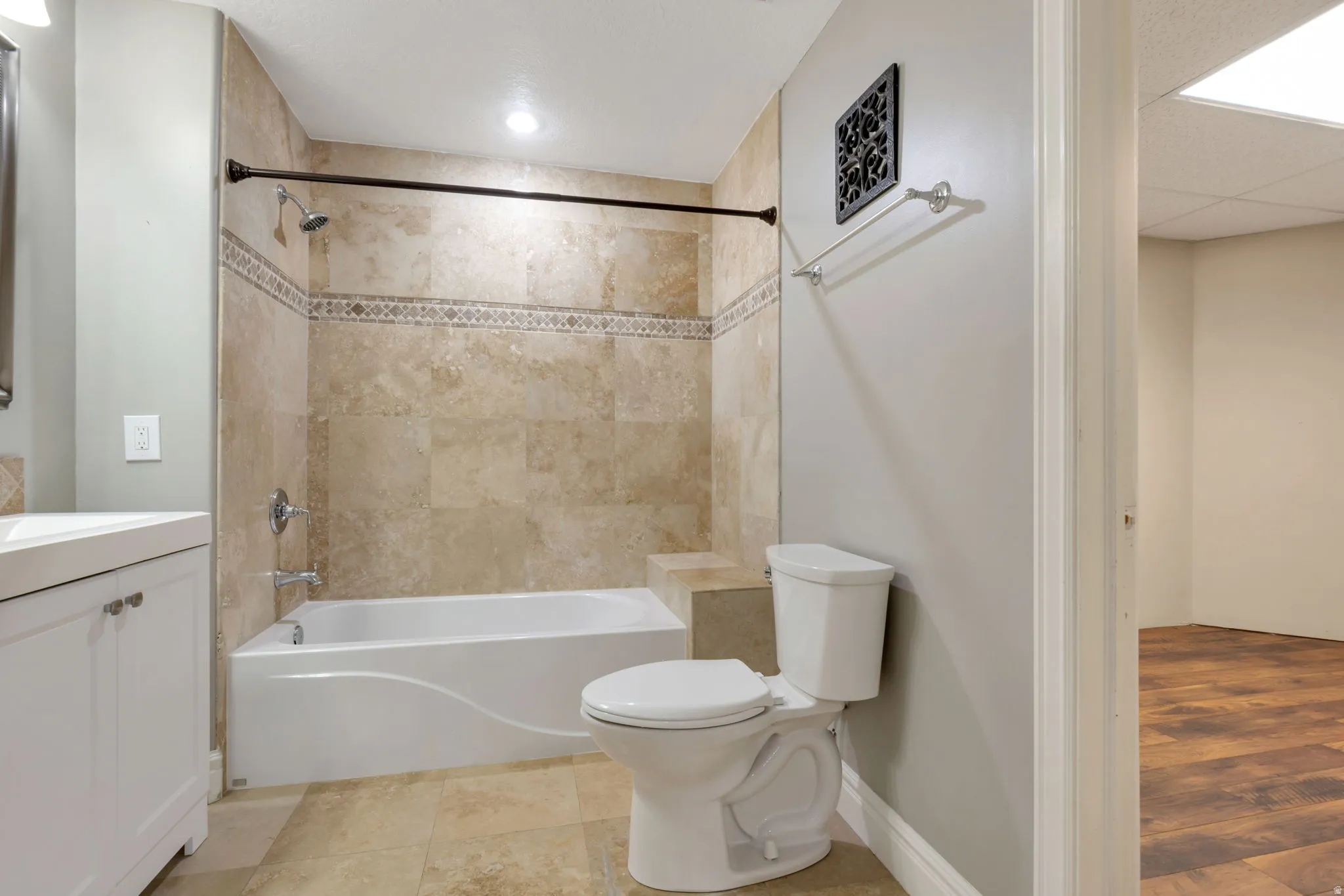 Full bathroom with a white vanity, white undermount sink, ceramic tile flooring, tiled shower surround with decorative accent band, and a built-in shower bench