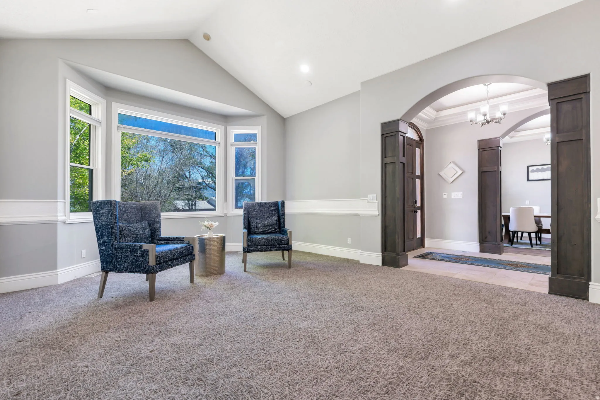 Bay window with white trim, vaulted ceiling, recessed lighting, and a broad arched entryway featuring dark wood-paneled columns
