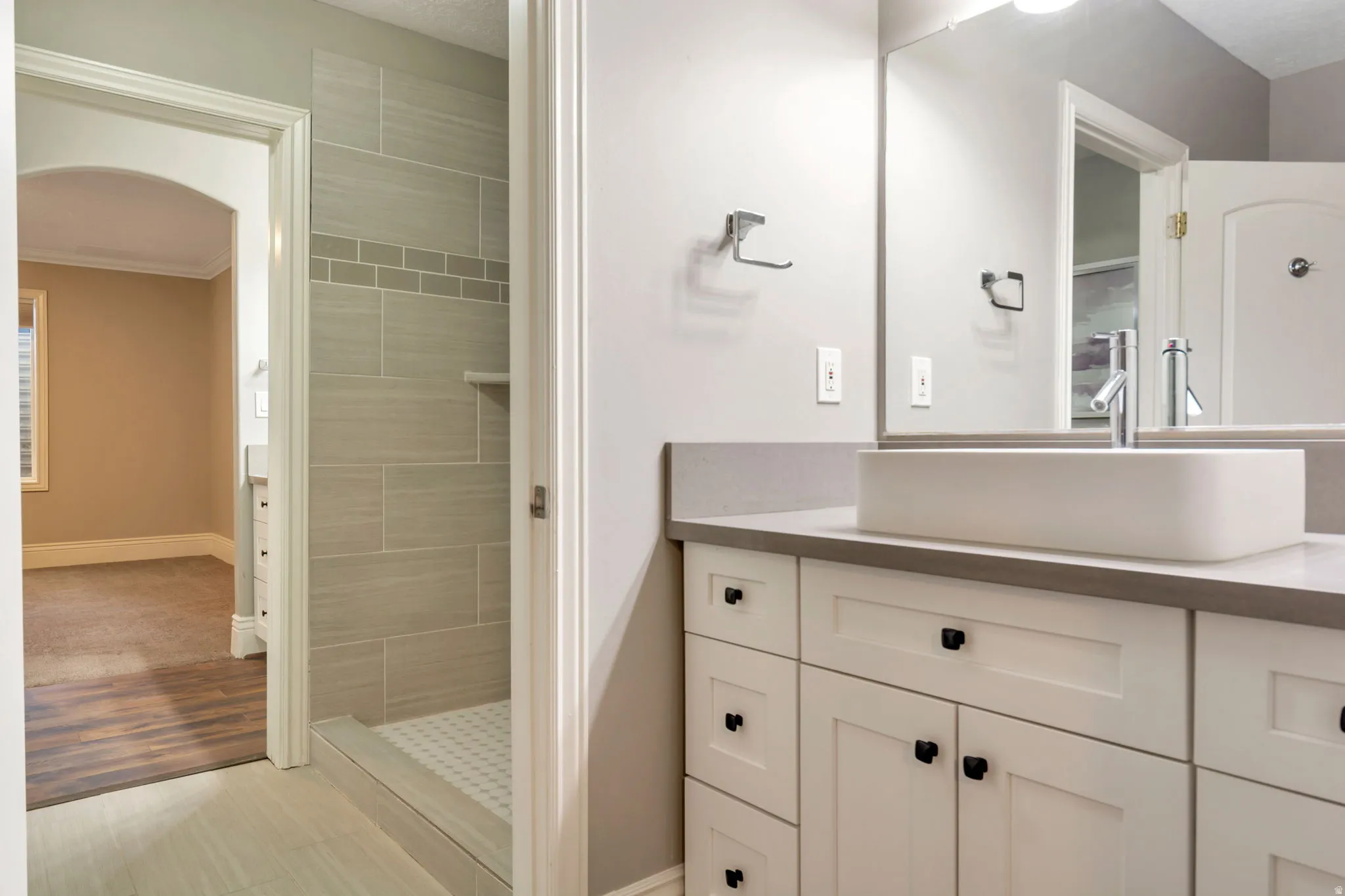 Dual vanity with white cabinetry and matte black hardware, rectangular vessel sink, polished chrome faucet, and expansive wall mirror