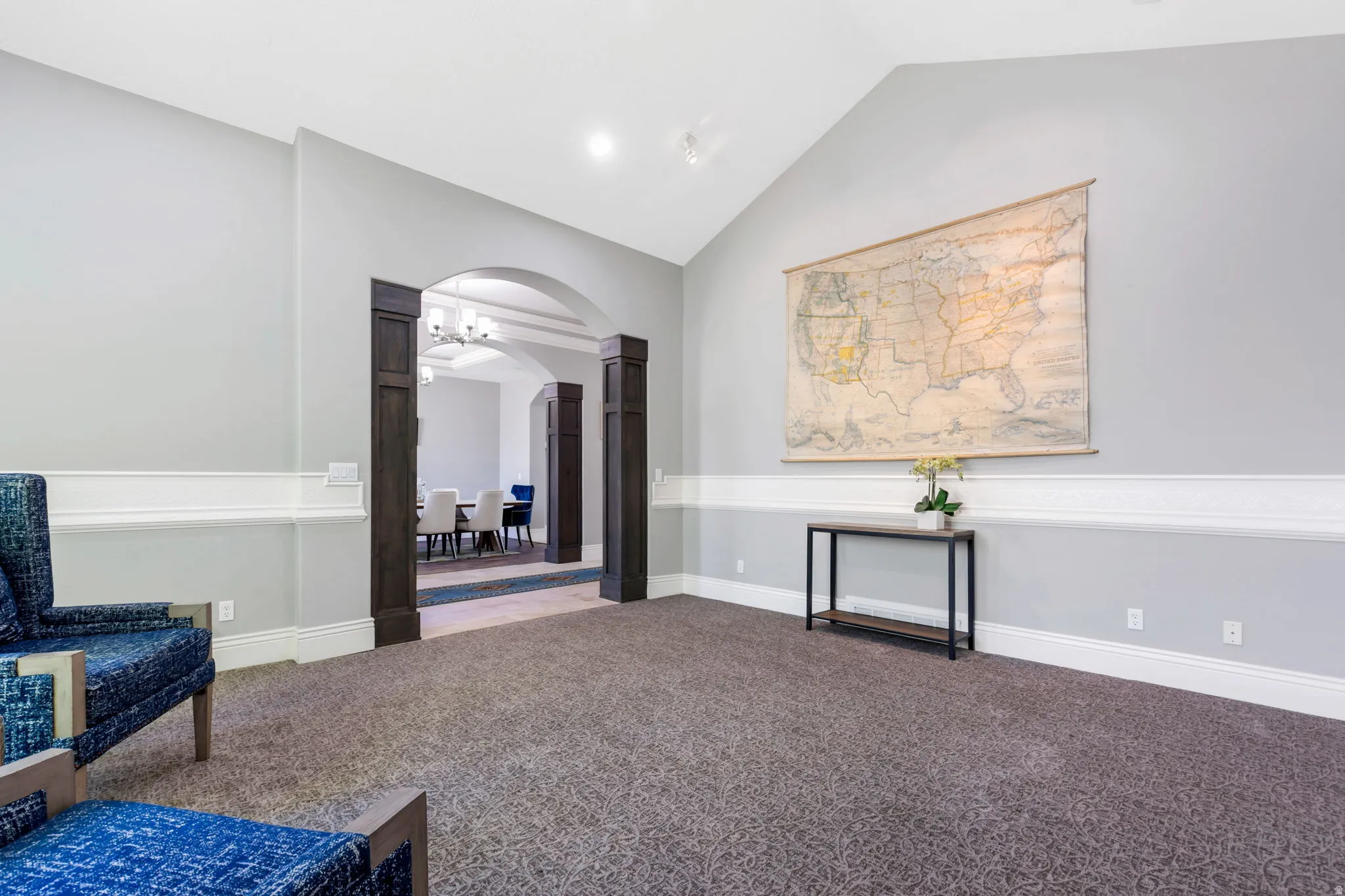 Vaulted ceiling, arched entryway, dark wood-finish columns, wainscoting, and patterned carpeting