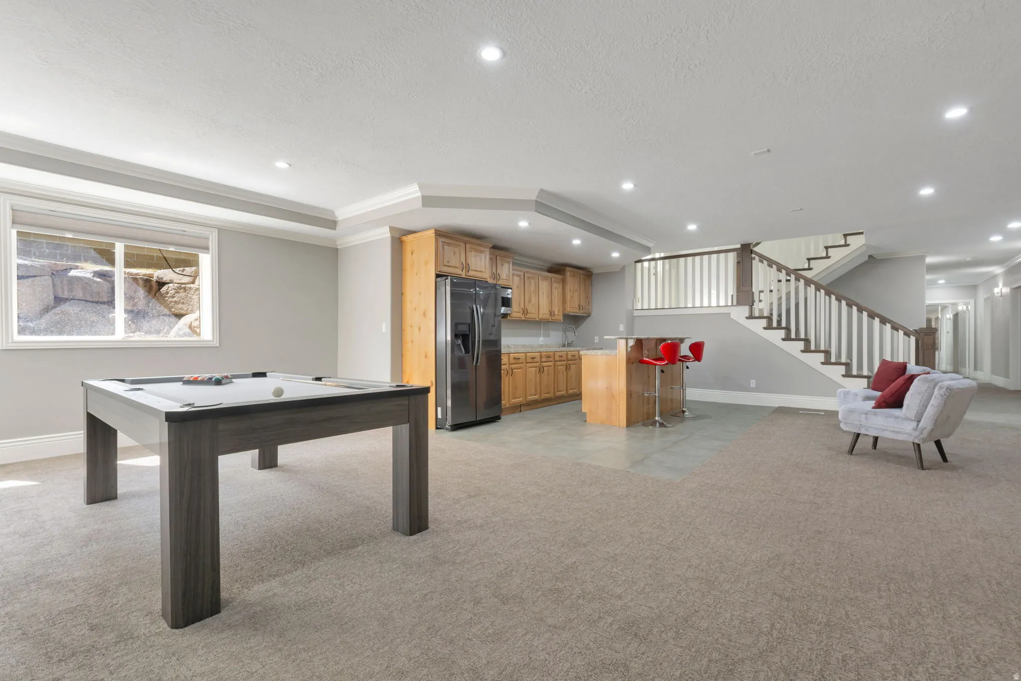 Spacious lower level featuring a built-in wet bar with wood-finish cabinetry, stainless steel appliances, and a staircase with white balusters