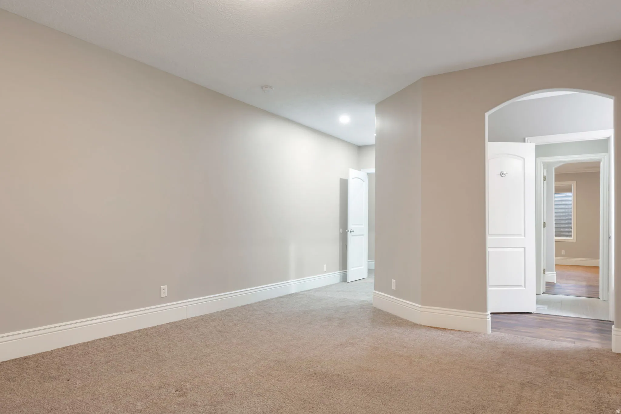 Carpeted flooring, arched doorway, recessed lighting, white trim, and neutral wall tones