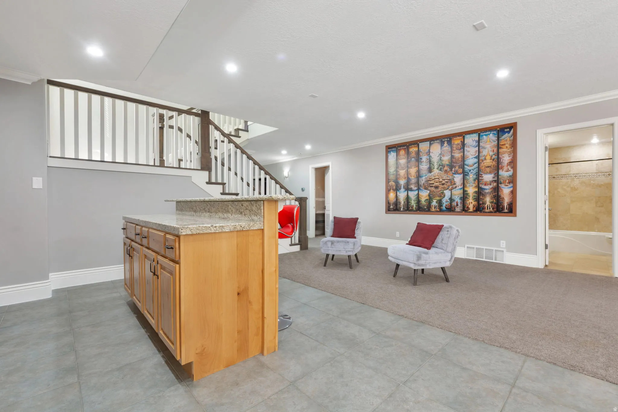 Wood-finish cabinetry with a light granite countertop, recessed lighting, carpeted flooring, tile flooring, and a staircase with white spindles and dark wood banister