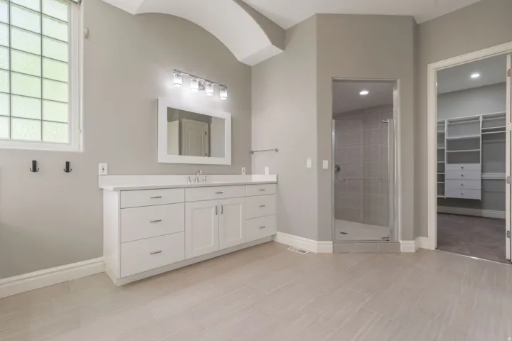 Elongated vanity with dual sinks, white cabinetry, and a light-colored countertop