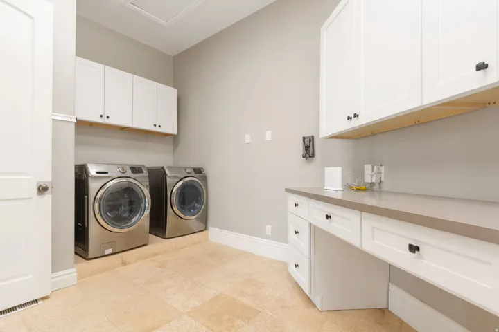 Light-toned tile flooring, white shaker cabinetry with dark hardware, integrated countertop workspace, and light gray wall paint