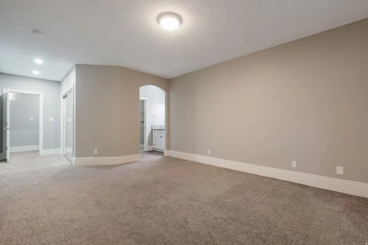Carpeted room with neutral wall tones, recessed lighting, and an arched entry to an adjoining space featuring a vanity