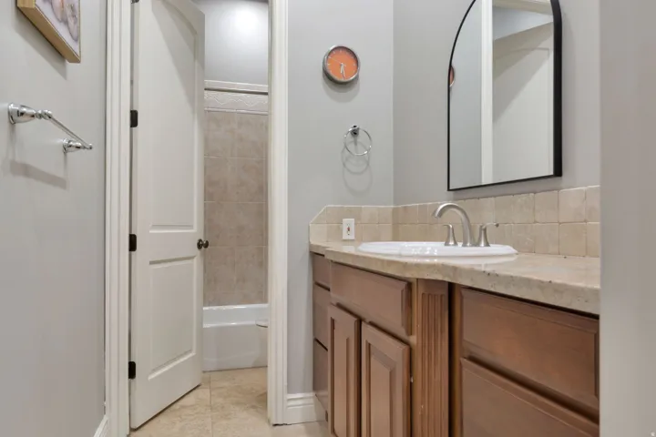 Bathroom featuring a wood-finish vanity with an integrated sink, stone countertop, and tile backsplash