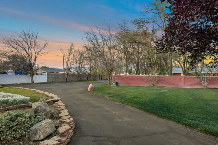 Paved driveway bordered by a stone-edged planter with mature shrubs, leading to a landscaped lawn