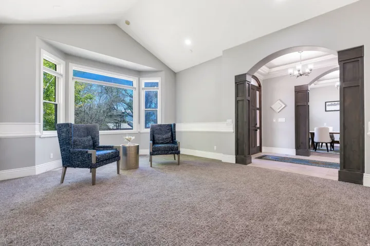 Bay window with white trim, vaulted ceiling, recessed lighting, and a broad arched entryway featuring dark wood-paneled columns