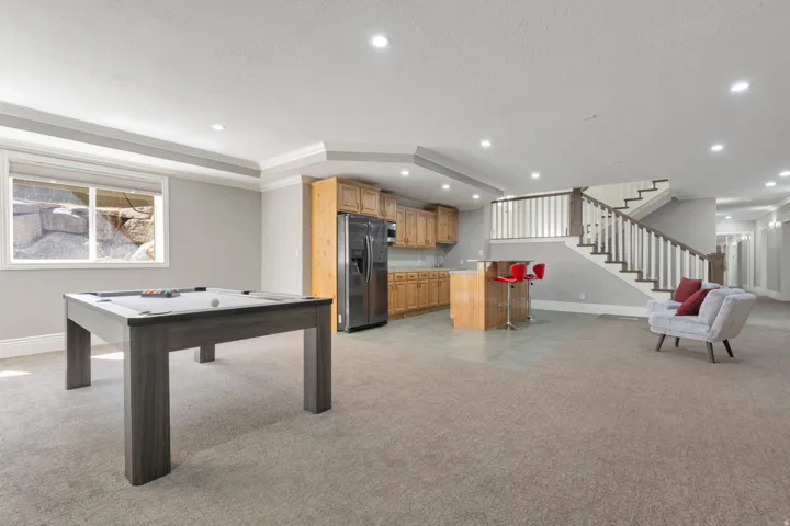 Spacious lower level featuring a built-in wet bar with wood-finish cabinetry, stainless steel appliances, and a staircase with white balusters